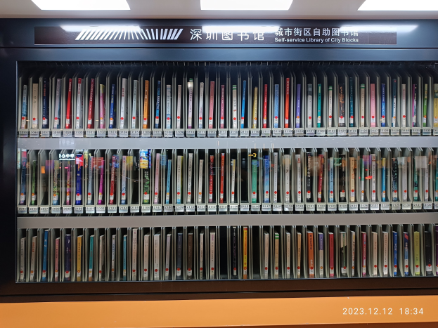 Eine gut beleuchtete Bibliothek mit Reihen von Bücherregalen, einem sichtbaren Textbrett und einem Wasserzeichen unten, das einer Selbstbedienungsbibliothek für Stadtviertel ähnelt.