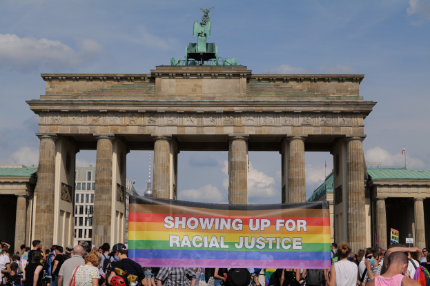 Eine Gruppe von Menschen steht vor dem Brandenburger Tor in Berlin, Deutschland, mit einer "Racial Justice"-Schlagzeile.