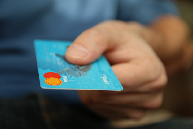 Person mit Kreditkarte in der Hand vor einem unscharfen Hintergrund.