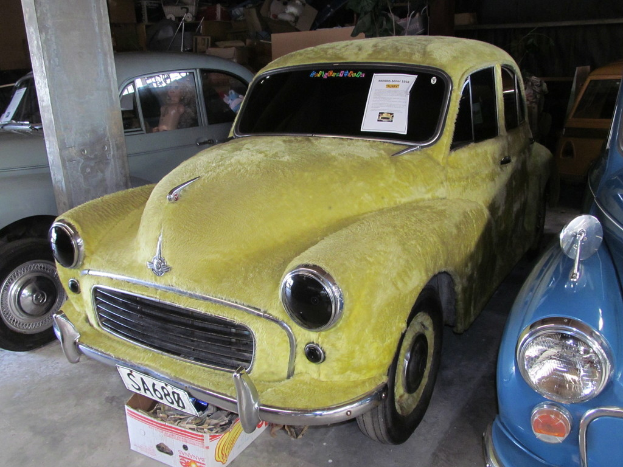 Mehrere Oldtimer vor einer mit Accessoires geschmückten Wand geparkt, mit einer Säule auf der linken Seite.