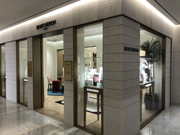 Eintritt in ein Boutique in einem Einkaufszentrum mit Glaswänden, Türen, Wandtext, Deckenleuchten, Stühlen, Tischen, einer Pflanze und sichtbarem Boden.