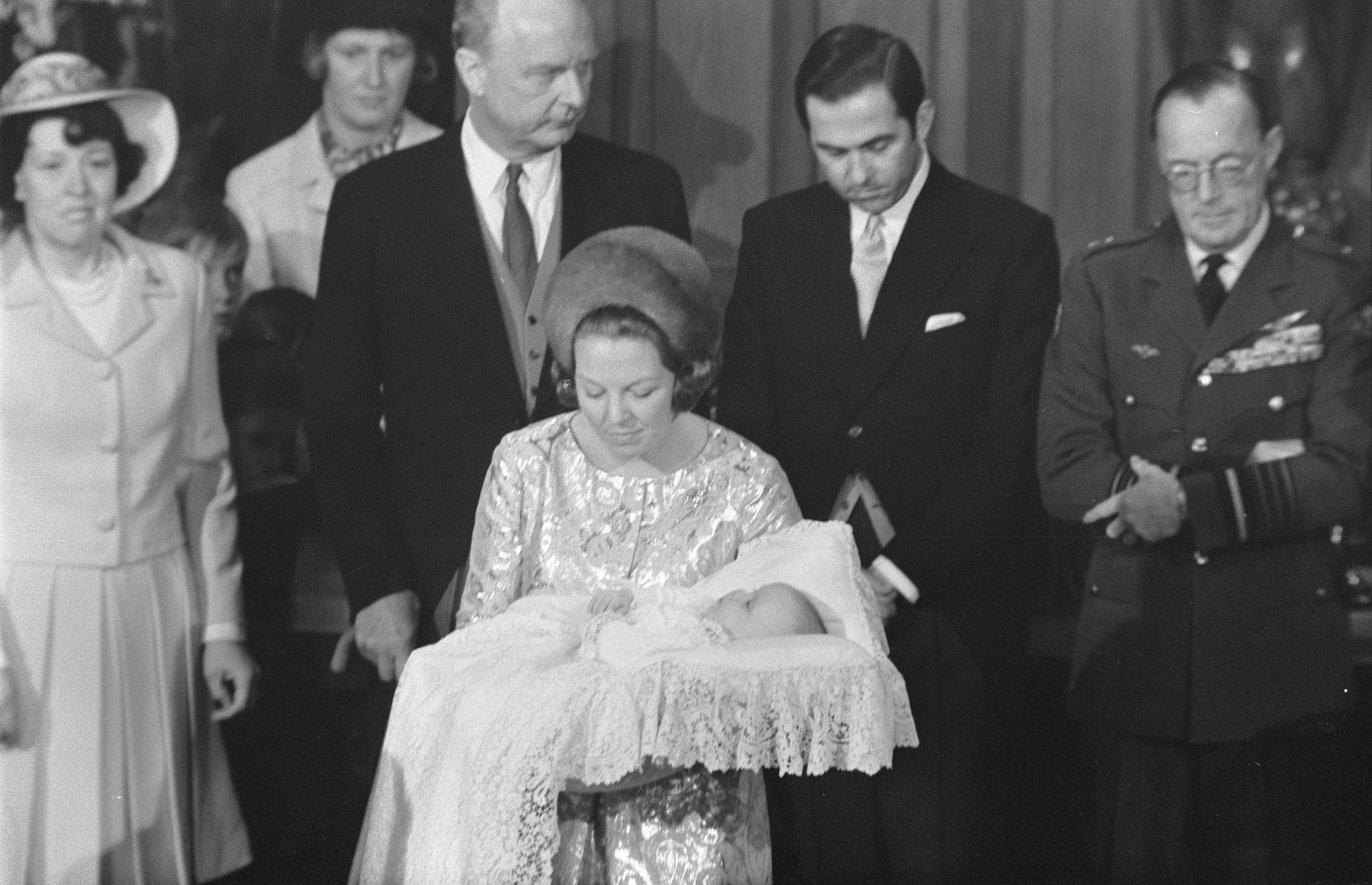 Königin Elizabeth II. wiegt ihren neugeborenen Sohn Prinz Philip, während Prinz Philip, Duke of Edinburgh, neben ihr in einem Anzug und Krawatte steht, mit Vorhängen im Hintergrund.