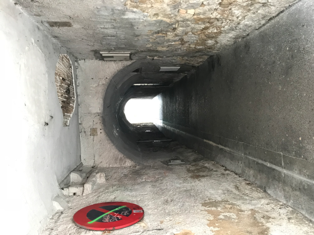 Ein Tunnel mit einem roten und schwarzen "Kein Eintritt"-Schild auf dem Boden, beleuchtet von Lampen an der Decke, das Teil eines Abwassersystems anzeigt.
