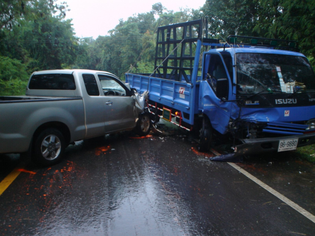 Ein schwerbeschädigtter Lkw mit eingedrückter Front und verbeulter Karosserie liegt am Straßenrand, umgeben von Bäumen unter einem klaren blauen Himmel.