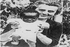 Ein Schwarz-Weiß-Foto einer Frau, die lacht, während sie ein Baby hält, mit Blättern im Hintergrund