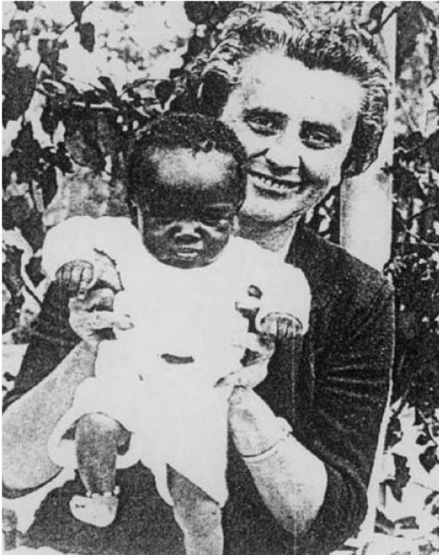 Ein Schwarz-Weiß-Foto einer Frau, die lacht, während sie ein Baby hält, mit Blättern im Hintergrund