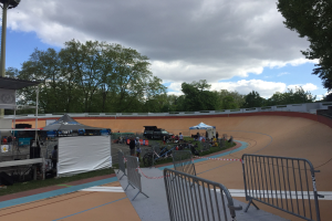 Gruppe von Radfahrern auf einer Schotterstrecke bei den 2018 UCI BMX-Weltmeisterschaften, mit Zuschauern, Zelten und Fahrzeugen im Hintergrund.