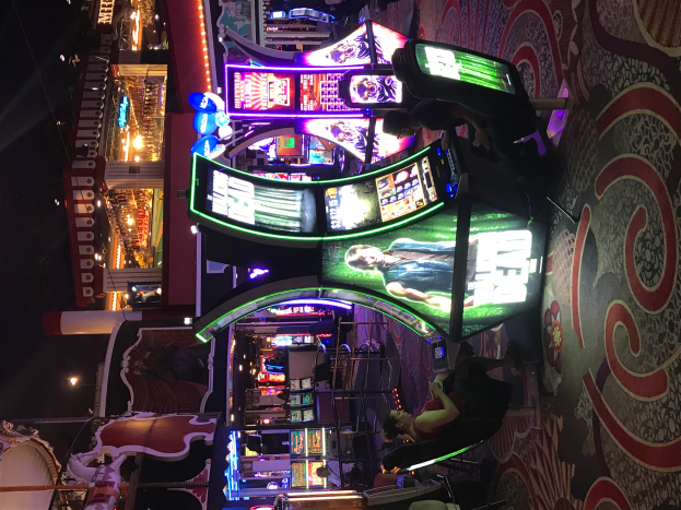 Eine Gruppe von Menschen, die in einem Casino an Spielautomaten spielt, mit beleuchteten Gebäuden im Hintergrund.