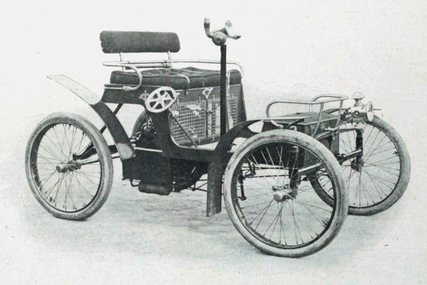 Ein Schwarz-Weiß-Foto eines frühen Elektroautos aus den 1900er-Jahren mit schlankem, aerodynamischem Design, großem runden Scheinwerfer, geschwungener Dachlinie, vier großen Rädern, einem prominenten Heckmotor, hellbezugener Sitzfläche und einem Armaturenbrett mit Knöpfen und Drehreglern.