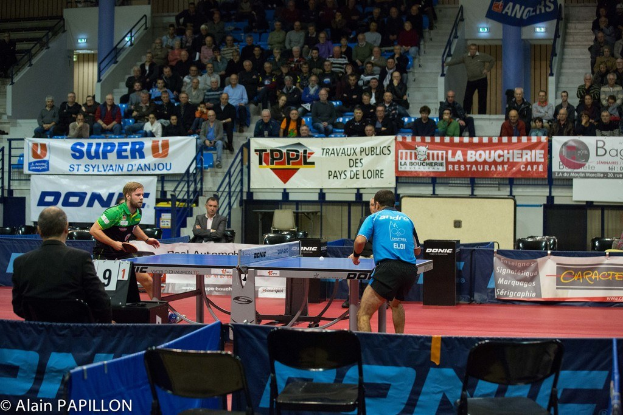 Indoor-Tischtennis-Match mit zwei Spielern und mehreren Zuschauern in einer Stadionatmosphäre.
