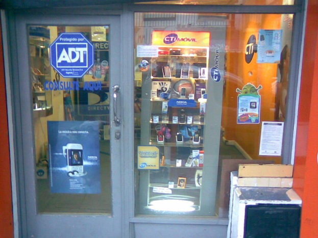 Ein mobiler Stand mit beschrifteten Glasvitrinen, die ordentlich mit Mobiltelefonen gefüllt sind, eine Wand und eine Tür mit einem Griff.