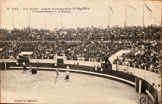 Schwarzes und weißes Foto eines Boxkampfes in einer Stadion mit Zuschauern auf den Rängen und einer Gruppe von Menschen in der Mitte.