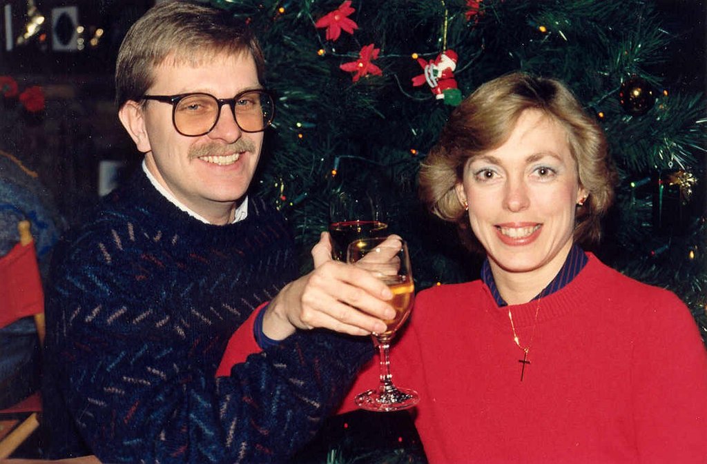 Ein Paar lächelt, waß Gläser in der Hand haltend, mit einem Weihnachtsbaum im Hintergrund.