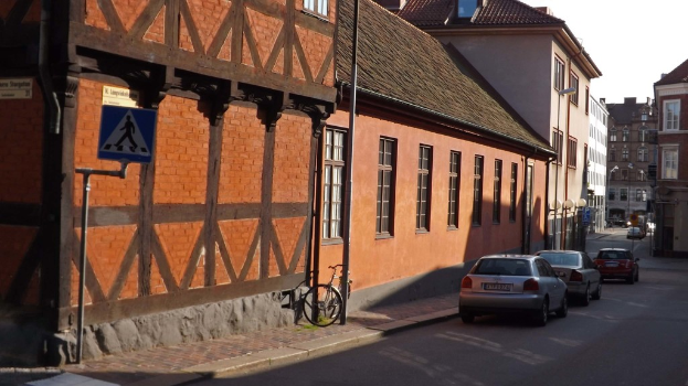 Fahrzeuge auf der Straße mit Gebäuden, Laternen, Verkehrsschildern, Fenstern und Dächern im Hintergrund und einem Fahrrad auf dem Fußweg in der Nähe eines Pfahls.