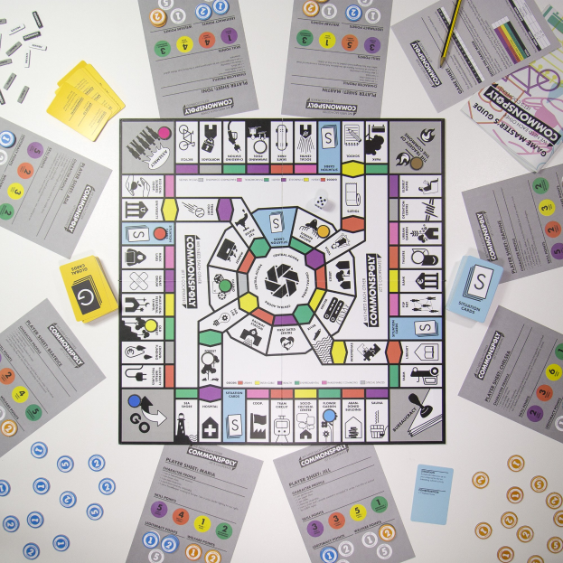 Ein Monopoly-Brettspiel, das auf einem Tisch mit verstreuten Spielkarten, Papieren und einem Bleistift darum herum aufgebaut ist.