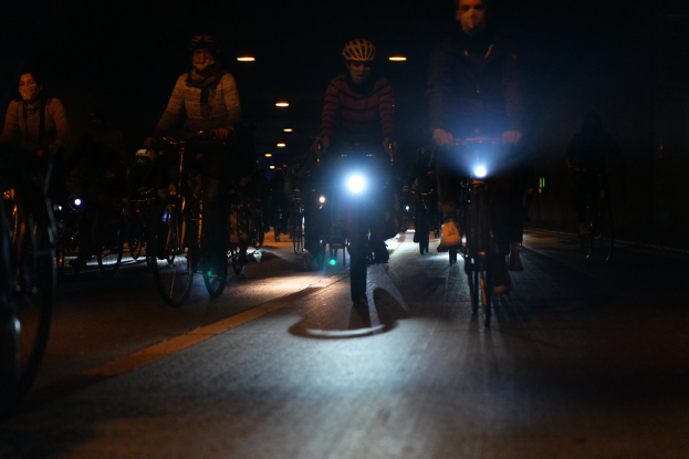 Eine Gruppe von Menschen, die nachts mit Fahrrädern durch eine Stadtstraße fahren, alle tragen Helme.