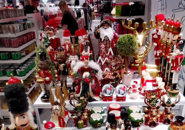 Ladeninnere voller Weihnachtsdekorationen, darunter Spielzeuge, Tassen und andere Gegenst├Ąnde auf Tischen und Regalen, mit Menschen, Lichtern und einer Wand im Hintergrund.