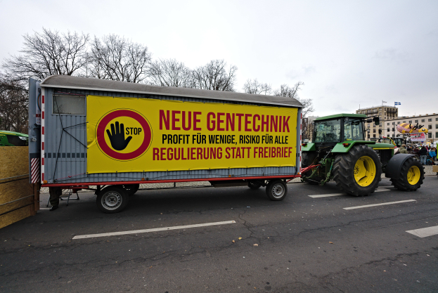 Ein Lastwagen mit einer Aufschrift auf der Rückseite fährt eine Straße in Deutschland entlang, umgeben von Menschen, Bäumen, Gebäuden und einem klaren blauen Himmel, wahrscheinlich Teil einer Demonstration.