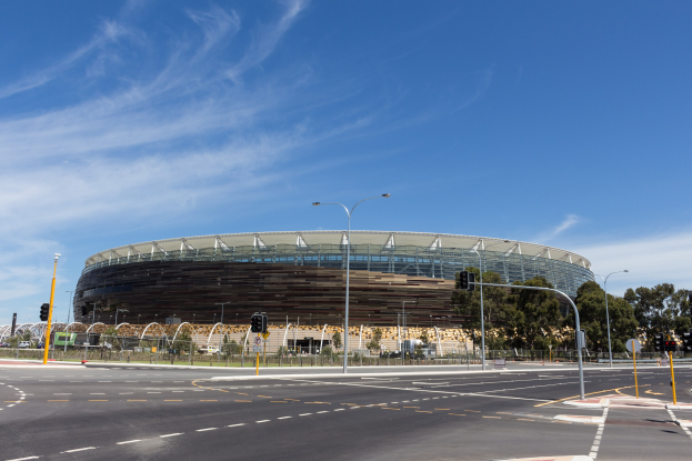 Großes Stadion mit starkem Verkehr davor, umgeben von Straßeninfrastruktur und Bäumen unter einem bewölkten Himmel.