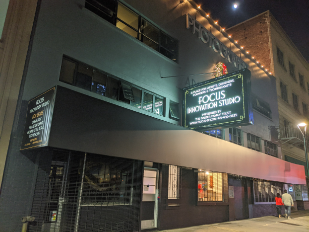 Außenansicht des Focus Innovation Studios in New York City bei Nacht, mit beleuchteten Gebäuden, Passanten auf dem Gehweg und sichtbarem Himmel.