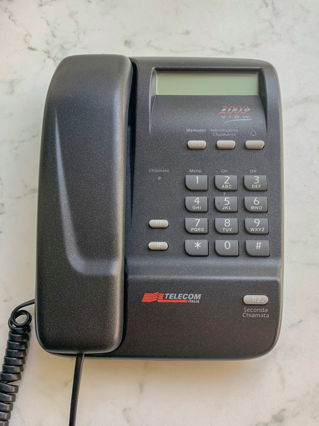 Ein schwarzes Telefon mit einer Zifferntastatur und einem angeschlossenen Kabel liegt auf einer weißen Marmorplatte.