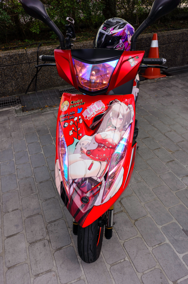 Ein oranges E-Scooter auf der Straßenseite mit einem Helm darauf, mit einer Verkehrskegel, einer Wand und Bäumen im Hintergrund.