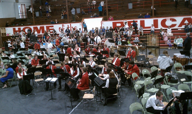 Eine Gruppe von Kindern sitzt auf Stühlen in einem Stadion während einer Musikstunde, mit Stadionplätzen im Hintergrund.