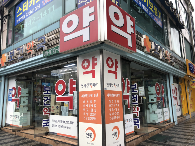Ein Gebäude mit Glaswänden und -türen, auf denen Schilder mit der Aufschrift "Südkoreas erste Apotheke in Seoul, Südkorea" stehen, sowie ein Schild an der Seite.