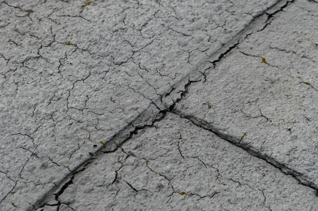Nahaufnahme einer gebrochenen, wetterfesten Straßoberflöche mit tiefen, breiten Rissen.