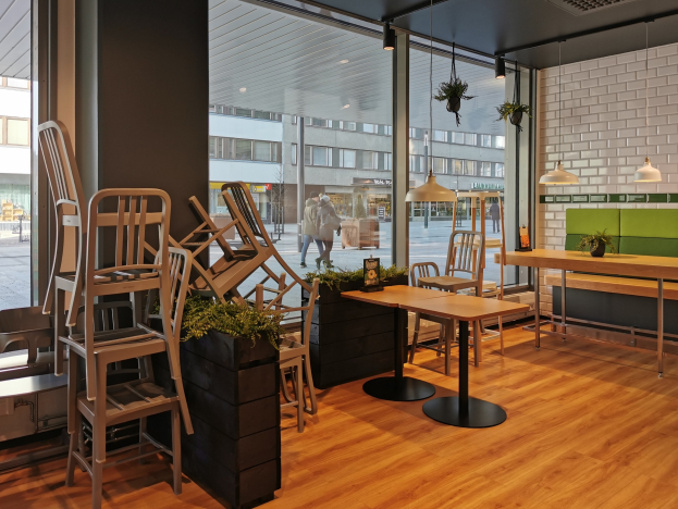 Ein Restaurant-Innenraum mit Holztischen und -stühlen, die durch ein großes Fenster zu sehen sind, das eine Stadtstraße mit Fußgängern, Gebäuden und Straßenelementen in Berlin, Deutschland, zeigt.