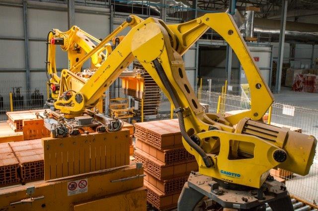 Großes Industriehochregallager mit gestapelten Kisten, Kränen, Zaun, Pfählen und einer fernen Wand in einer Fertigungsanlage.