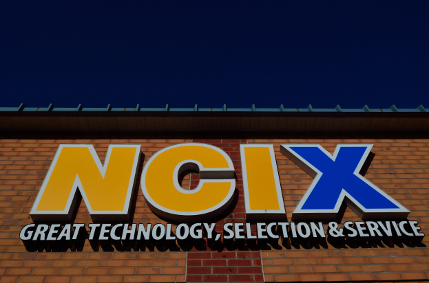 Ein Ziegelgebäude mit einer Tafel, auf der "NCIX Große Technologie, Auswahl und Service" steht, unter einem klaren blauen Himmel.