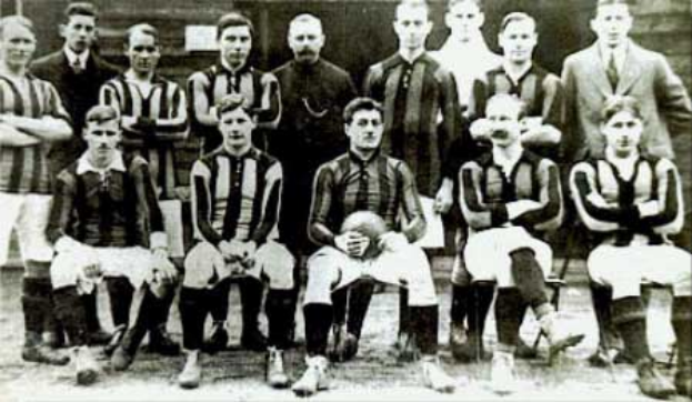 Ein Schwarz-Weiß-Foto einer Fußballmannschaft, einige stehen und einige sitzen, vor einer Wand, mit dem Text "Ballymena Football Club" unten.