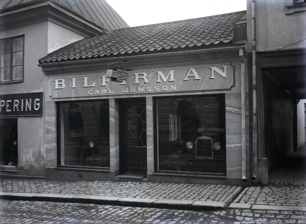 Ein Schwarz-Weiß-Foto eines Gebäudes mit einer 'Bilferman'-Aufschrift, Fenstern, einer Tür und Tafeln mit Text sowie einer Straße unten.