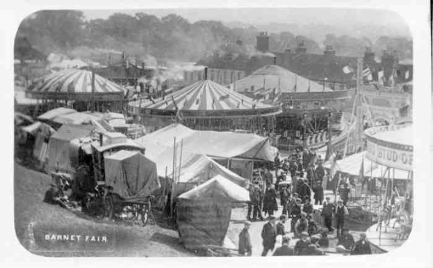 Ein altes Schwarz-Weiß-Foto einer lebhaften KarnevalsSzene mit Zelten, Menschen, Karren, Polen, Bäumen und Gebäuden im Hintergrund, beschriftet mit "Barnet Fair, London, England".