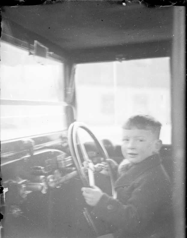 Ein junger Junge in Schwarz und Weiß sitzt im Fahrersitz eines Autos und hält das Lenkrad mit konzentrierter Miene.
