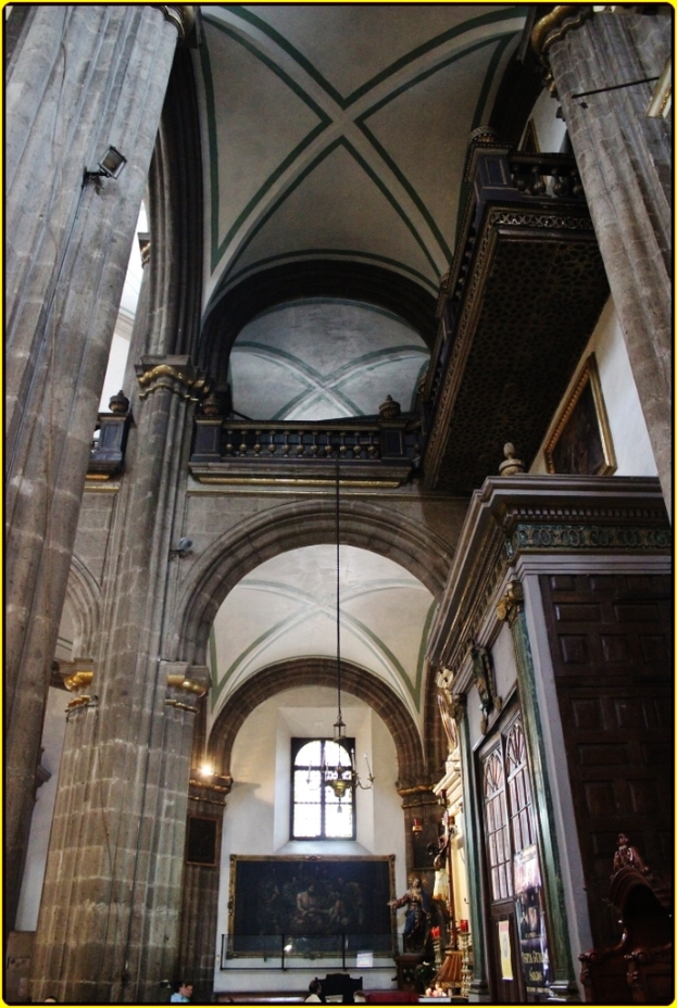 Ein Innenblick in ein Schloss mit Schränken, beleuchteten Säulen, Wandskulpturen, einem großen Rahmenbild und einer Deckenleuchte.
