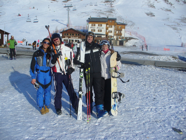 Vier Personen posieren für ein Foto mit Skate-Pads und Werkzeugen vor einer schneebedeckten Berglandschaft.