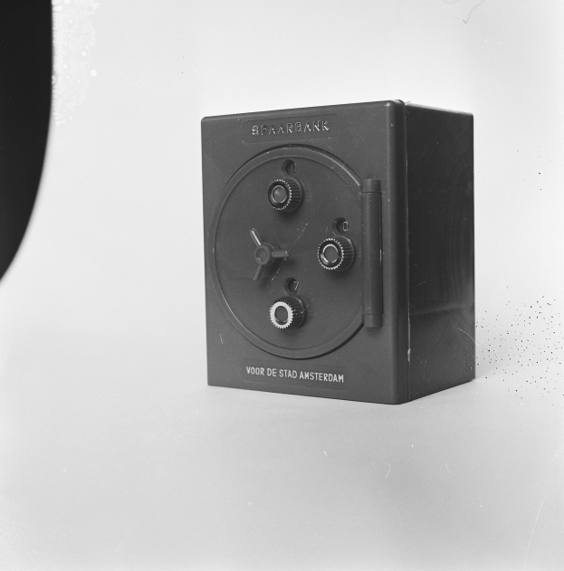 Ein Schwarz-Weiß-Foto einer rechteckigen Sicherheitsschachtel auf einer weißen Oberfläche, mit einem Griff oben, einem Schloss vorne und einem Schlüsselloch in der Mitte.