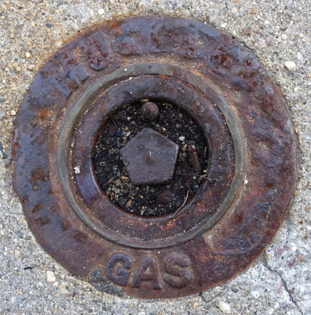 Rostiger Metallschachtdeckel auf dem Boden mit der Aufschrift "Gas".