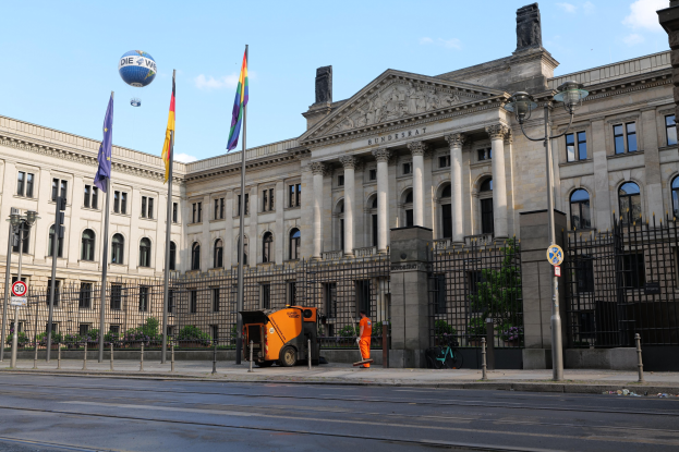 Großes modernes Gebäude mit vielen Fenstern, als Bundestag in Berlin, Deutschland identifiziert, umgeben von Straßeninfrastruktur, Fußgängern und Flaggen.