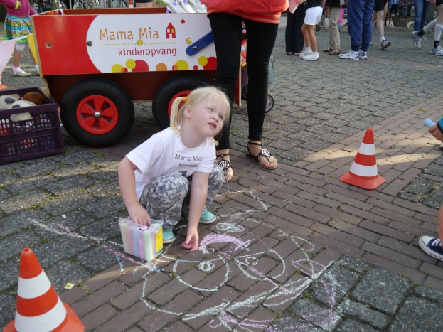 Menschen gehen und stehen auf einem Gehweg mit Absperrgittern, einem Wagen und einem Plastikbehälter, während ein Kind in der Nähe in der Hocke sitzt; ein Auto mit einigen Gegenständen im Inneren ist ebenfalls sichtbar.