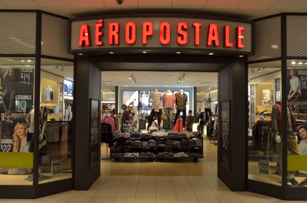 Innenansicht eines Aeropostale-Ladens in einem Einkaufszentrum mit Schaufensterpuppen in Kleidern, Kleiderständern, Infotafeln, Glaswänden, Beleuchtung und einer sichtbaren Decke sowie einem Schild mit der Aufschrift 'Schließung im Juni'.
