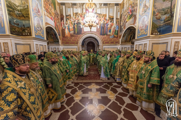 Gruppe von Priestern in grüner und goldener Gewandung, die in einer Kirche mit bemalten Wänden, einem Kronleuchter und einem Bogen im Hintergrund während einer St. Petersfeier stehen.