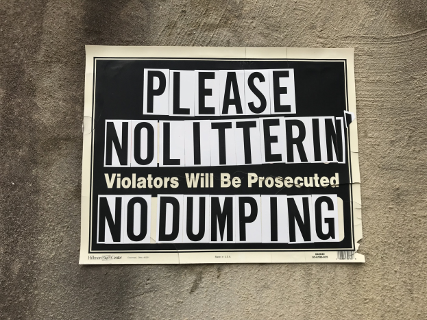 Schwarz-weißes Schild an einem Gebäude mit der Aufschrift "Bitte keine Verschmutzung - Verursacher werden verfolgt - Keine Ablagerung".