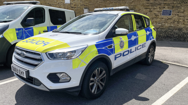 Zwei Polizeiwagen nebeneinander auf einem Parkplatz geparkt mit einer Tafel an einer Wand dahinter.