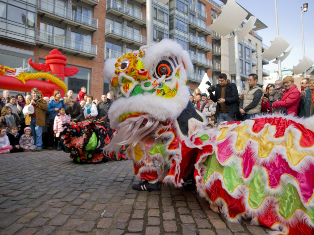 Vibrantes chinesisches Neujahrsfest in Amsterdam mit Löwen tanzen und Menschenmenge vor Gebäuden und klarem blauen Himmel.