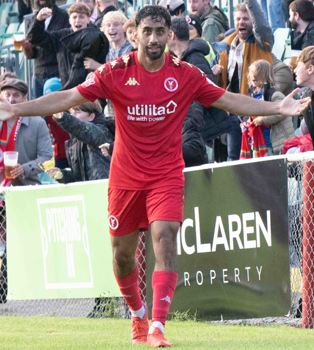 Ein Fussballspieler in roter Uniform rennt mit ausgebreiteten Armen auf einem Feld, mit einer Menge und einem Banner mit der Aufschrift "Middlesbrough FC v Swansea City - Sky Bet Championship" im Hintergrund.