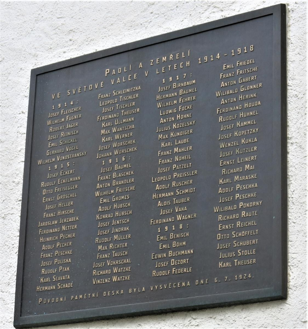 Tafel aus dunklem Material mit der Inschrift "Gedenktafel für die Opfer des Holocaust" in fetter Schrift, umgeben von einem dekorativen Rahmen, an einer Gebäudewand angebracht.