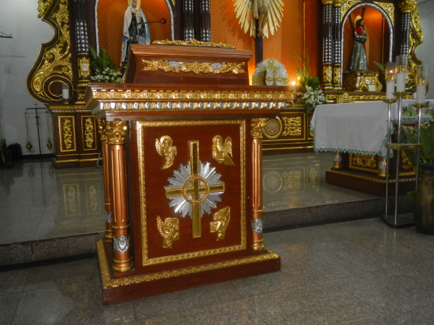 Ein Altar in einer Kirche mit einem Kreuz, Statuen, Blumensträußen, Kerzen, einem tuchbedeckten Tisch und anderen Gegenständen, an den Wänden mit Lichtern geschmückt.